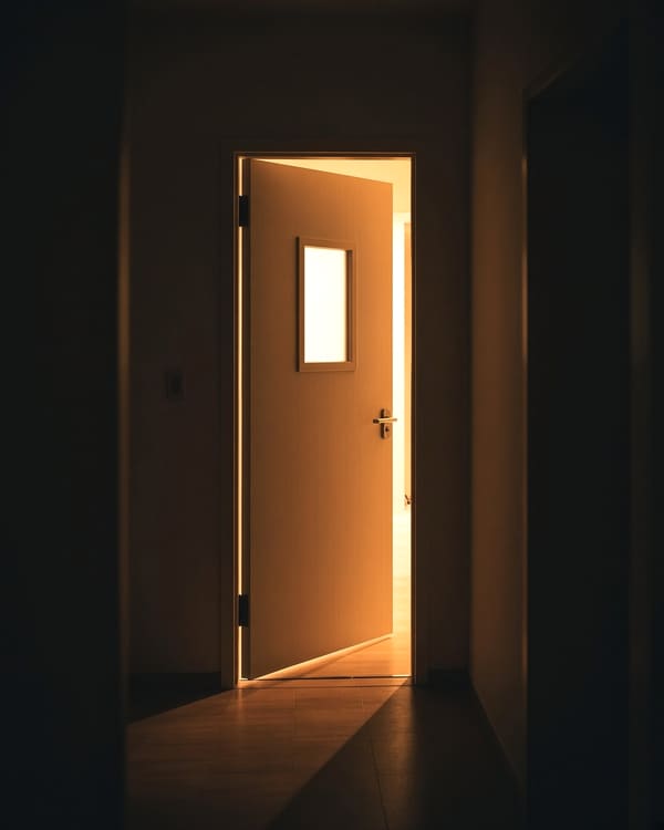 A part-open door with warm light across a dark hallway floor.